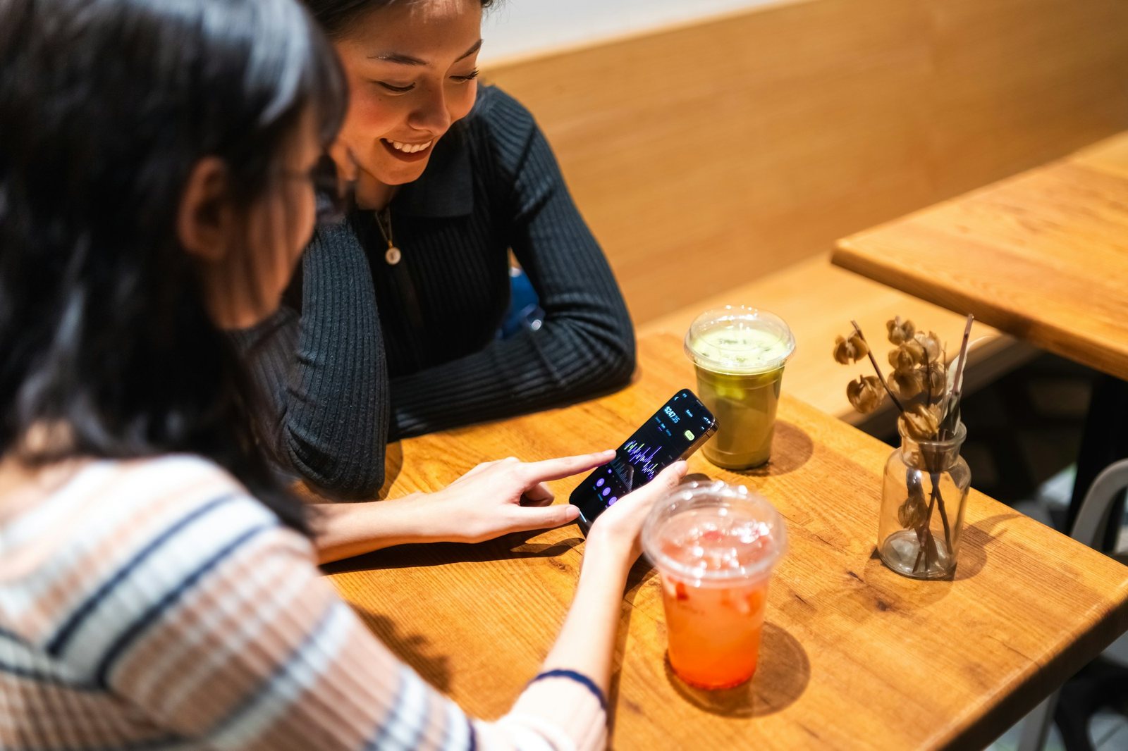 Two friends at a café table, laughing at something on a phone